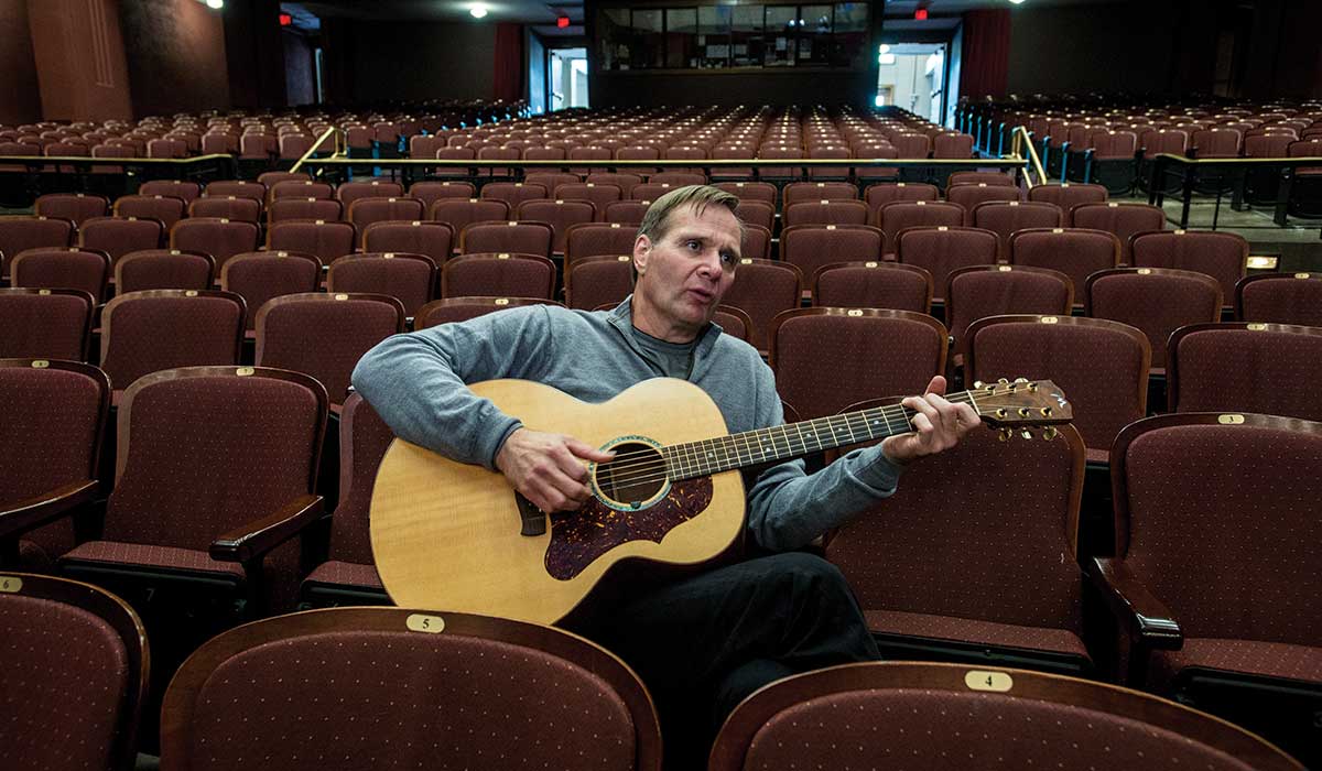 Tim Ryan Rouillier picks his guitar while chatting inside UM’s Dennison Theatre. Ryan, a country music artist in Nashville originally from tiny St. Ignatius, will debut his symphonic memoir, “Play Me Montana,” inside the same theater on June 17. (Photo by Todd Goodrich)