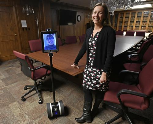Professor Sara Rinfret poses with a robot in a classroom